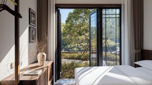 A bedroom with a bed, a wooden desk, a vase with dried plants, and a large window with a view of trees and a road. - ALOR VALLEY HUZHOU (Huzhou)