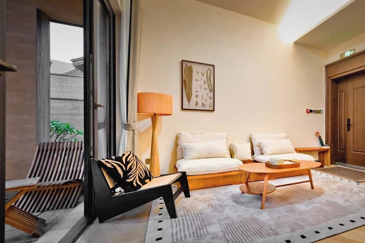 Una sala de estar moderna con un sofá, una mesa de centro y una silla. Se ve una puerta y una ventana al fondo.