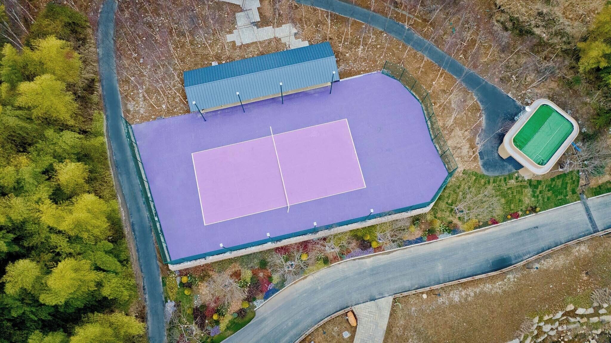 Luftaufnahme eines Sportplatzes mit einer umlaufenden Straße und Grünflächen.
