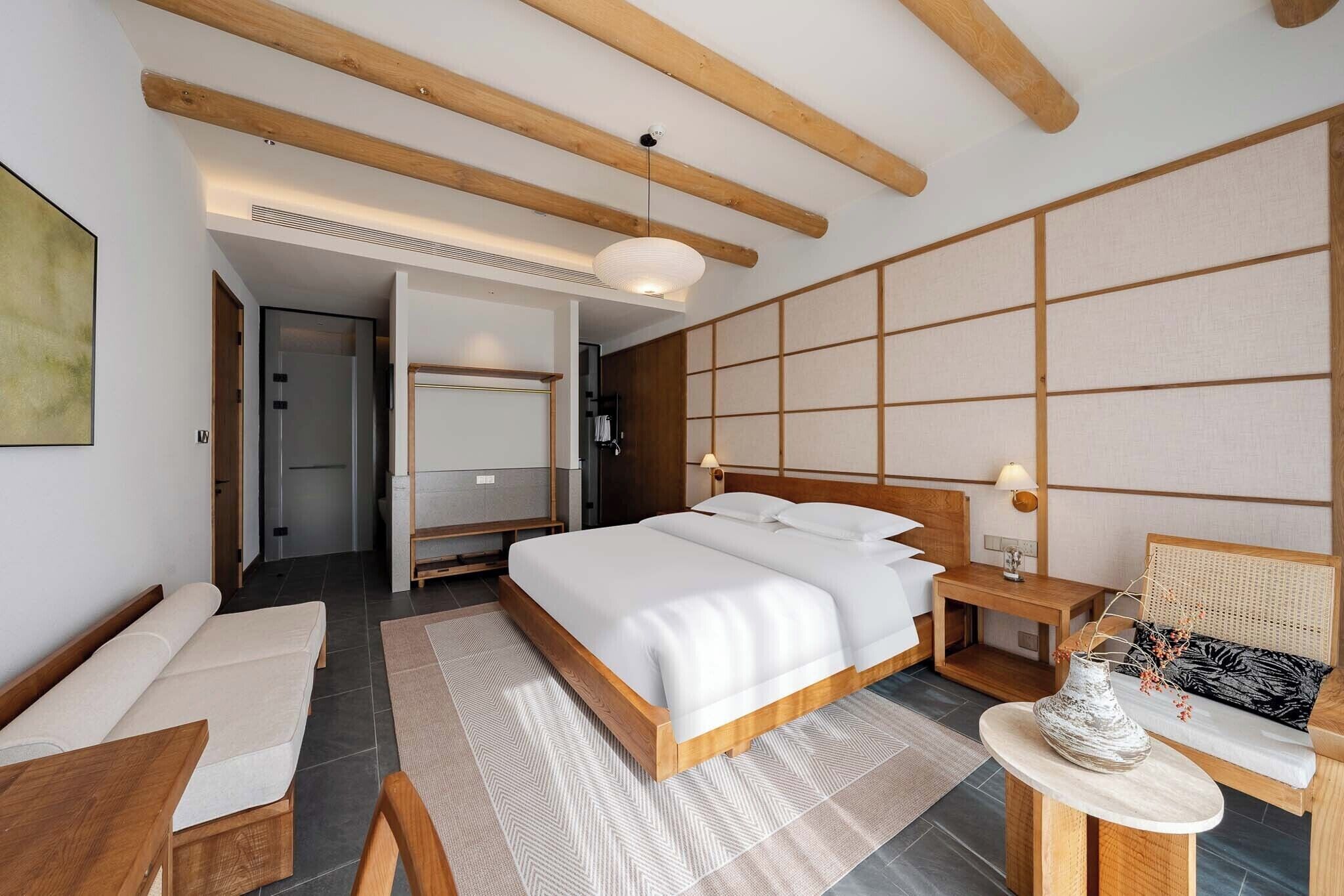 Una habitación de hotel moderna con una cama de madera, mesitas de noche, un sofá y un muro con paneles de tatami.