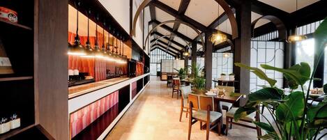 A restaurant with a long counter, wooden beams, and potted plants.