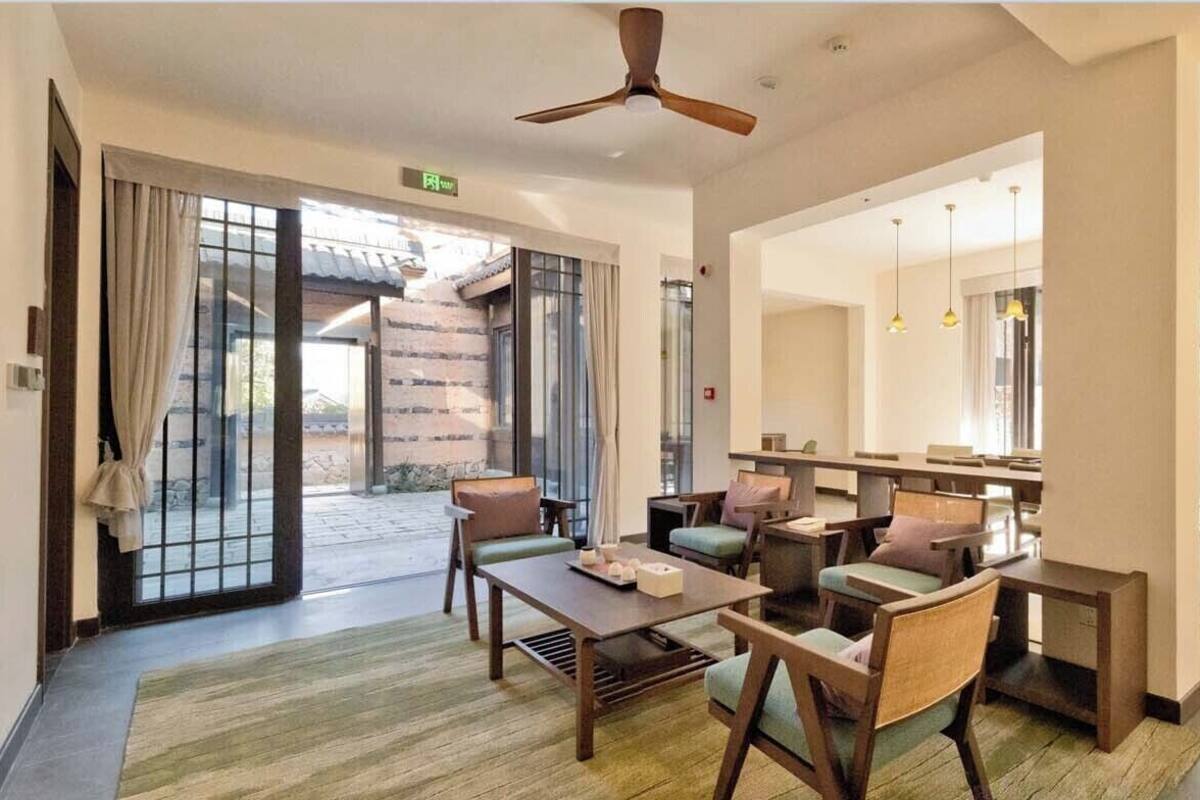 Un hall de hotel con zona de estar, ventilador de techo y vistas a través de puertas de vidrio.
