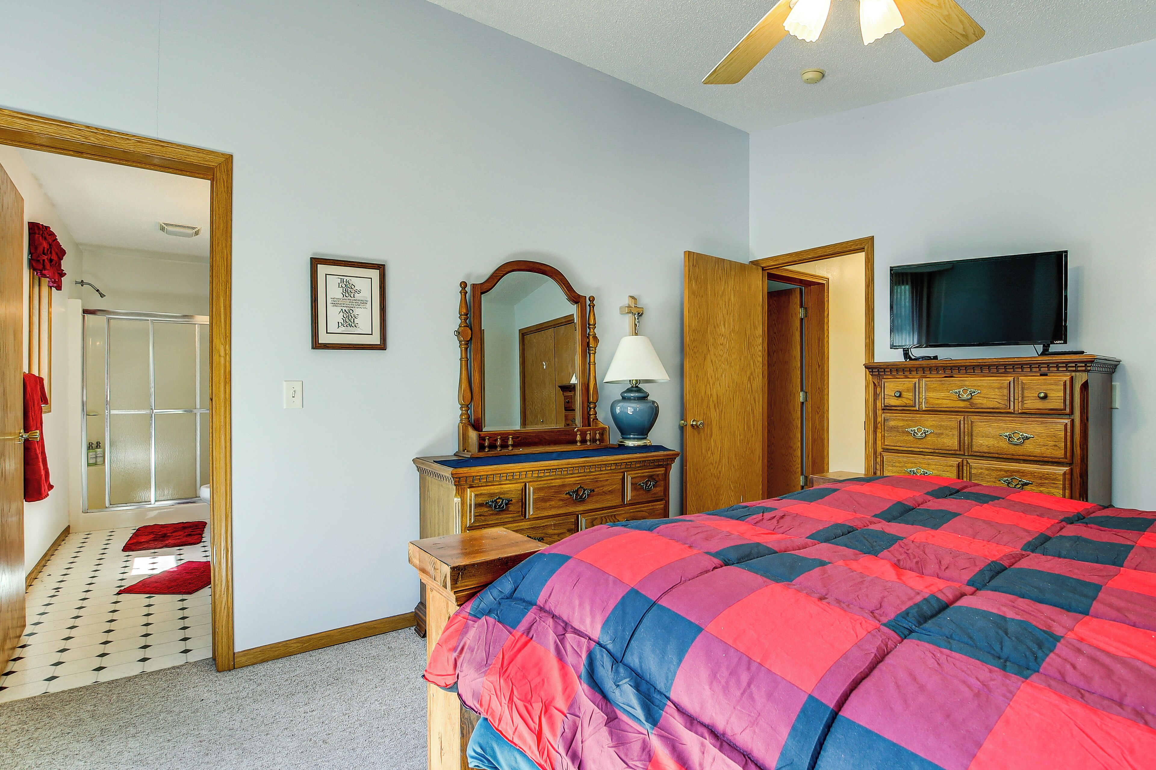 A bedroom with a bed, a dresser, a television, a mirror, and a door leading to a bathroom.