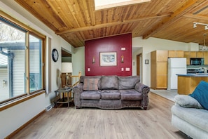 Ein Wohnzimmer mit Holzboden, einer roten Akzentwand, einem braunen Ledersofa und einer Küche im Hintergrund.