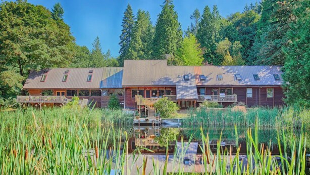 A lodge with a central building and two wings, surrounded by a pond and dense forest.