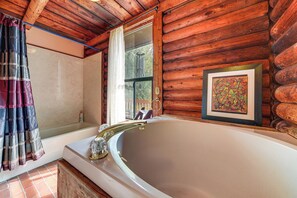 A log cabin bathroom with a bathtub, a shower, and a window with a view.