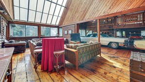 A spacious room with a high ceiling, wooden flooring, a large window, a red table, and a vintage car in the background.