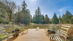 A wooden deck with metal chairs and a bench, overlooking a pond surrounded by trees.