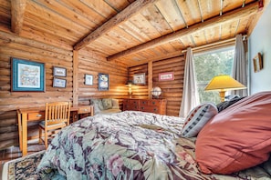 Habitación de cabaña de troncos con cama, escritorio de madera y cuadros en las paredes.