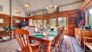 A wooden interior with a dining table, chairs, a television, and a fireplace.