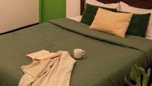 Una habitación con una cama, una puerta verde, una ventana con cortina y un accesorio de iluminación.