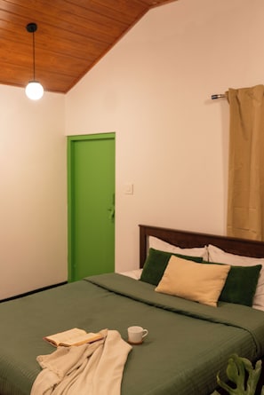 Une pièce avec un lit, une porte verte, une fenêtre avec un rideau et un luminaire.