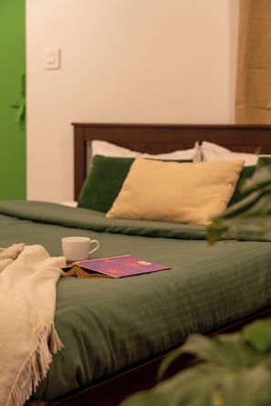 Ein Bett mit grüner Bettwäsche, einer weißen Tasse und einem Buch.