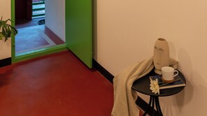 Una habitación con una puerta verde, una pequeña mesa con una taza y un libro, y dos cuadros en la pared.