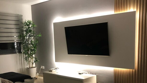 Uma sala de estar moderna com uma televisão de tela plana na parede, um console minimalista e um sofá.