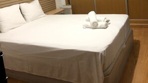 Cama bem arrumada com lençóis brancos, cabeceira de madeira e guarda-roupa de madeira com portas deslizantes.