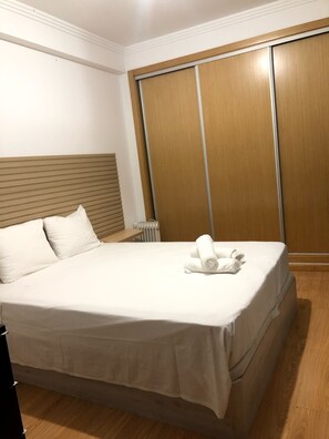 Ein ordentlich bezogenes Bett mit weißer Bettwäsche, einem Holz-Kopfteil und einem Holzschrank mit Schiebetüren.