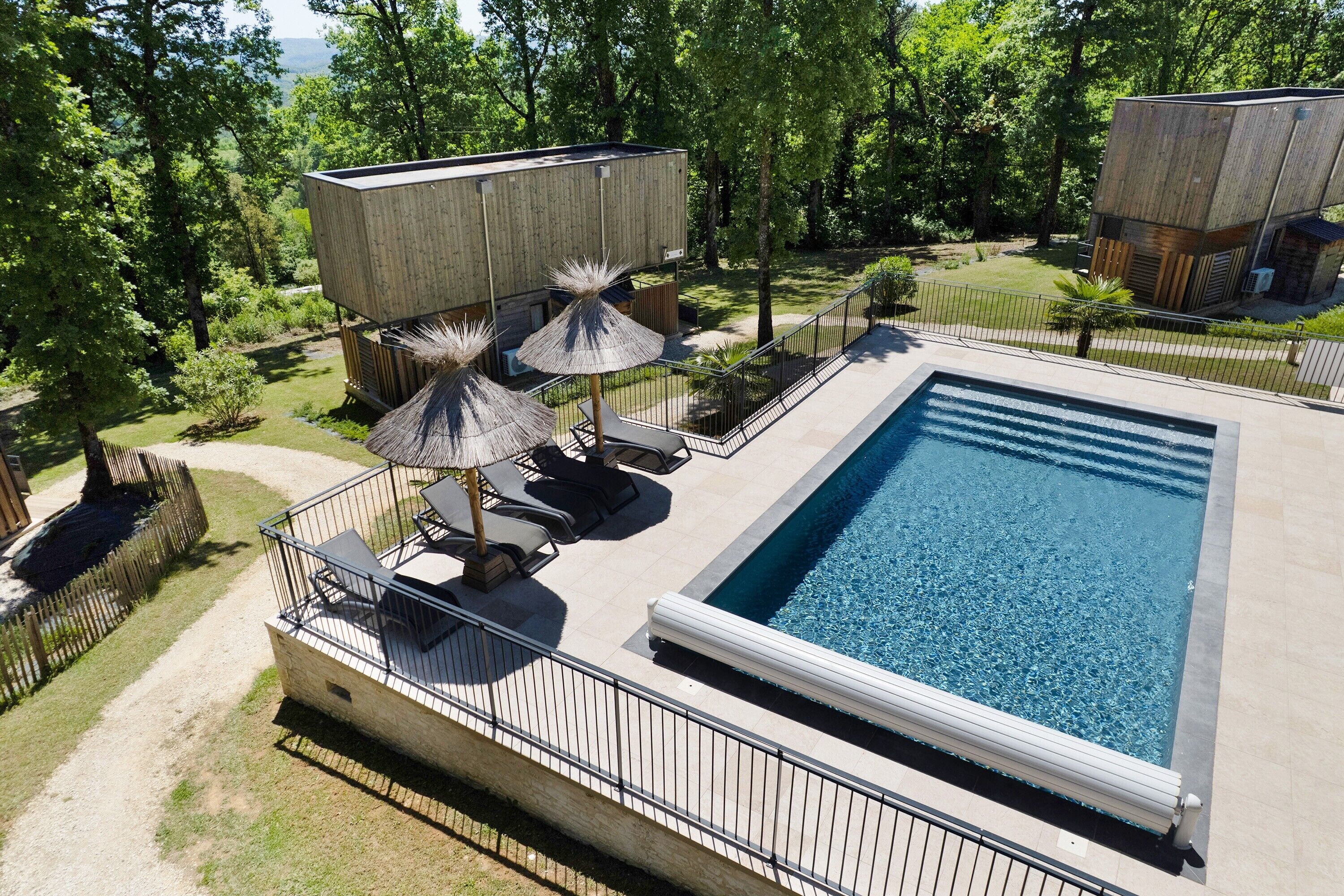 A swimming pool with a deck, surrounded by a wooden fence, and a view of the surrounding forest.