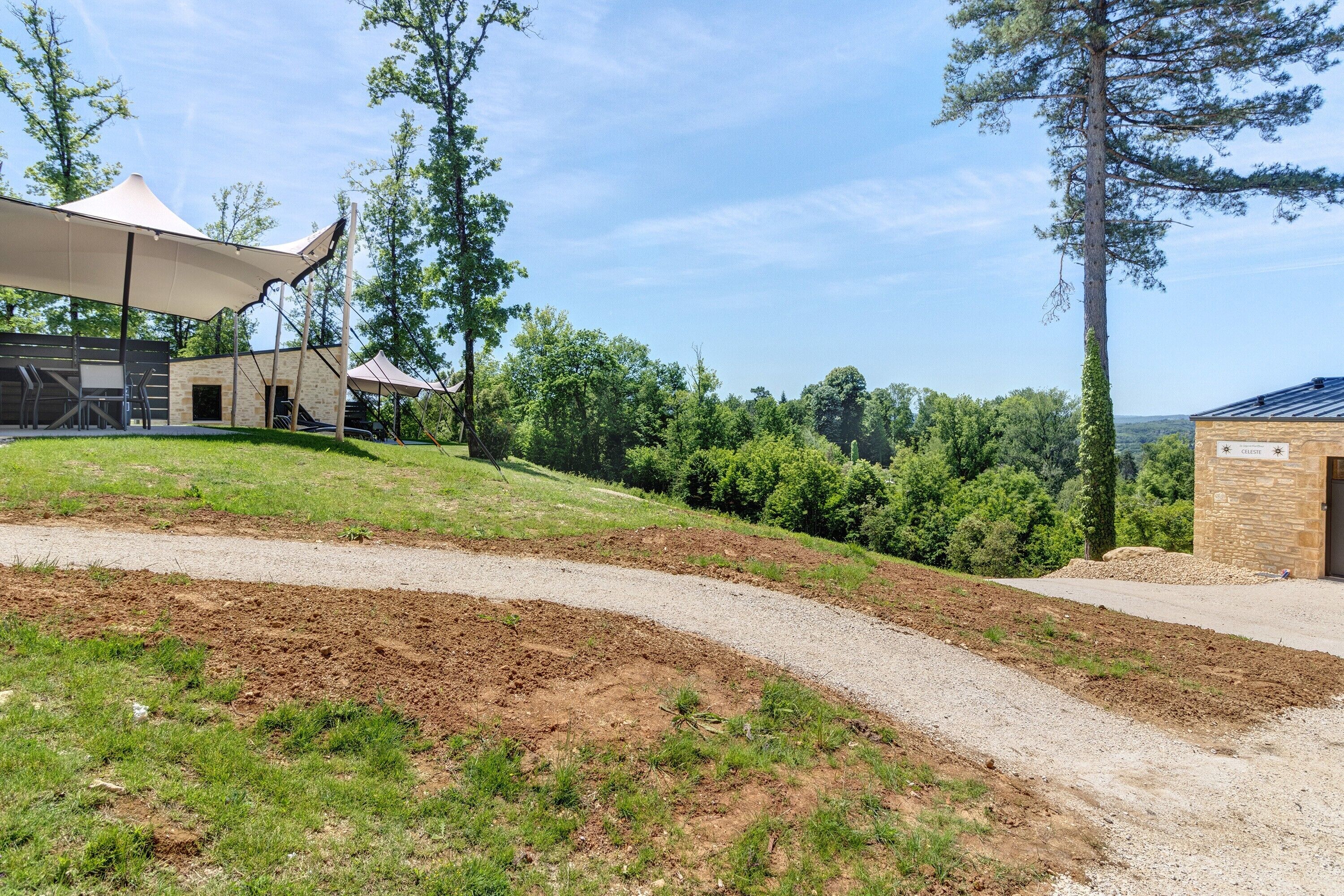 A paved path leading to a building with a stone facade, surrounded by greenery and trees.