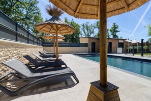 Uma área à beira da piscina com espreguiçadeiras, guarda-sóis de palha e vista desobstruída para a piscina.