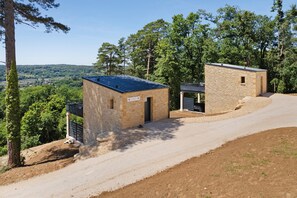 Um edifício de pedra com dois andares, com um caminho de paralelepípedos, rodeado por árvores e uma paisagem acidentada.