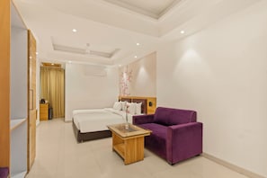 Una habitación de hotel moderna con una cama, un sofá morado, una mesa de centro de vidrio y un armario de madera.