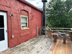 A red building with a wooden deck, a window with blinds, and a door.
