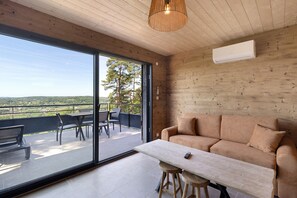Um interior moderno com teto de madeira, um sofá, uma mesa e vista para um pátio exterior através de uma porta de vidro.