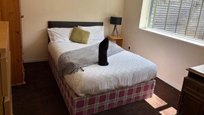 A bedroom with a bed, a nightstand with a lamp, a window with blinds, and a wardrobe. - Lovely 1-bedroom house in charming Limerick for a relaxing stay (Limerick)