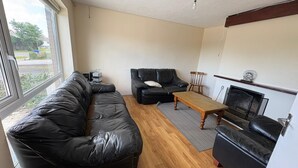 A living room with a black leather sofa, a wooden coffee table, a fireplace, and a window with a view of the outside. - Lovely 1-bedroom house in charming Limerick for a relaxing stay (Limerick)