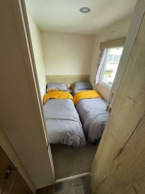 Ein kleiner, schmaler Raum mit zwei Betten, einem Fenster und einer Tür.