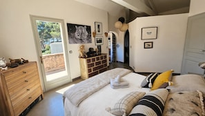 Ein Schlafzimmer mit einem Bett, einer Holzkommode, einer Tür, die auf einen Balkon führt, und einer Wand mit gerahmten Bildern.