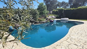 Ein Schwimmbecken mit Steinrand, umgeben von Grünpflanzen und einem Zaun.