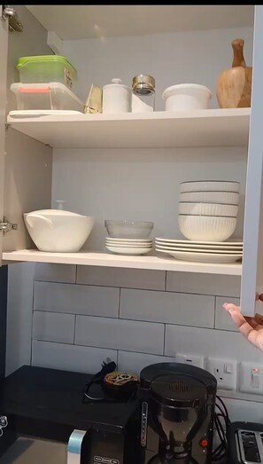 Eine Küche mit weißen Schränken, einer Kaffeemaschine und verschiedenen Geschirr- und Aufbewahrungsbehältern.