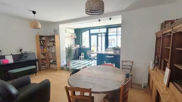 Un comedor con una mesa redonda, sillas, una lámpara colgante, una estantería y vistas a una cocina.