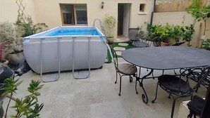 Una piscina exterior con un jacuzzi cubierto, una mesa con sillas y plantas en macetas.