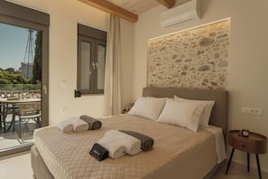 A bedroom with a large bed, a stone wall, and a view through a glass door. - Casa Dianthos, Elegant Home for Families & Groups in Pigi, Rethymno (Pigi)