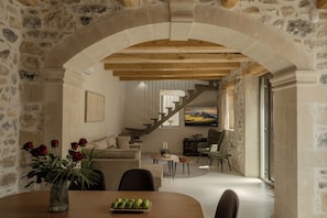 A stone-walled room with a wooden dining table, a vase of red roses, and a staircase leading to another level. - Casa Dianthos, Elegant Home for Families & Groups in Pigi, Rethymno (Pigi)