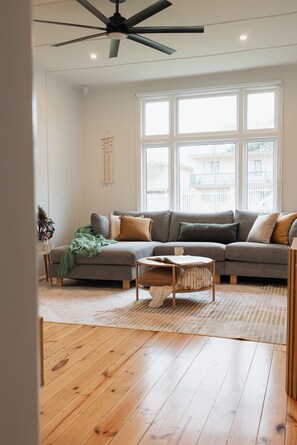 Ein Wohnzimmer mit grauem Sofa, Couchtisch, Holzboden und Deckenventilator.