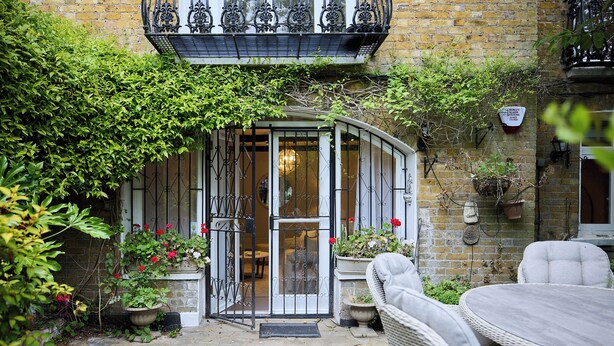 A stone-paved courtyard with a curved entrance, wicker furniture, and potted plants. - The Brick & Timber Flat by Abbey Road (London)