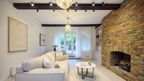 A living room with a fireplace, a sofa, a coffee table, and a view through a glass door. - The Brick & Timber Flat by Abbey Road (London)