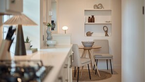 A modern kitchen with a dining area, featuring a round table, two chairs, a bowl, and a shelf with decorative items. - The Brick & Timber Flat by Abbey Road (London)