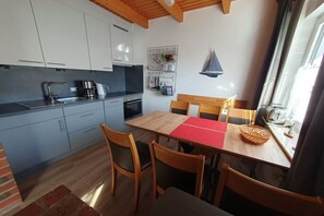 A compact kitchen with modern appliances, a dining area with a red table runner, and a window with curtains. - Holiday home in Hooksiel with swimming pool (Hooksiel)