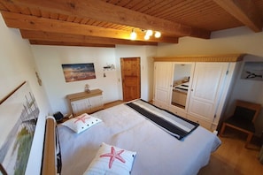 A bedroom with a bed, wooden ceiling beams, a wardrobe, a mirror, and a painting on the wall. - Holiday home in Hooksiel with swimming pool (Hooksiel)