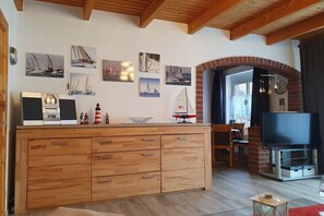 A spacious living area with a wooden cabinet, a television, and sailboat-themed wall art. - Holiday home in Hooksiel with swimming pool (Hooksiel)