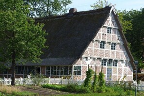 Ett traditionellt hus med halmtak, ett vitt staket, stora fönster och en symmetrisk fasad.