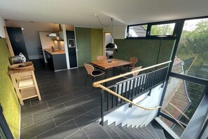 En modern inredning med ett matområde, kök och en trappa som leder upp till en balkong.