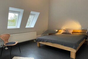Ett sovrum med en säng, två fönster, en stol och ett element.