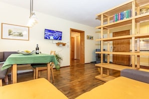A living room with a wooden bookshelf, a dining table with chairs, a television, and a framed picture on the wall. - Holiday apartment in Waidring with Wi-Fi (Waidring)