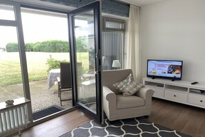 Ein Wohnzimmer mit einer Couch, einem Fernseher und einer Schiebetür zu einem Außenbereich.